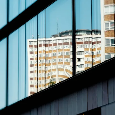 Glass facade reflecting a high-rise under blue sky. Lookout