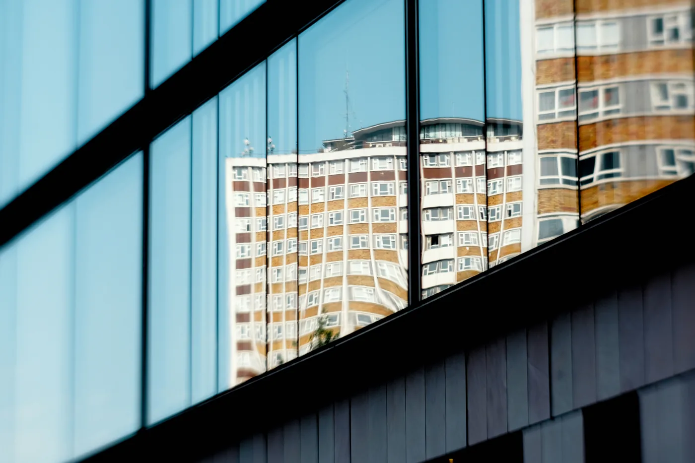 Glass facade reflecting a high-rise under blue sky. Lookout